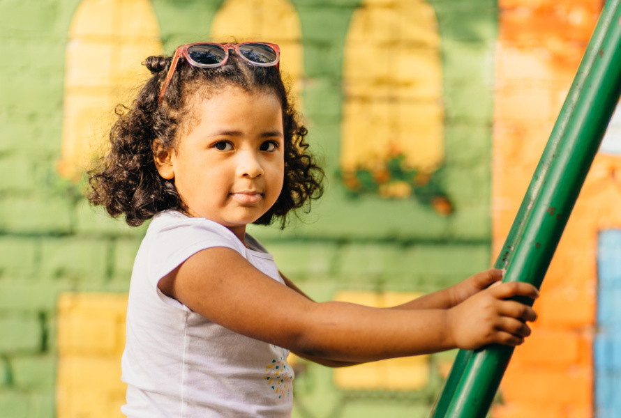 Cute preschooler girl playing on playground in summer day. Colorful backround.