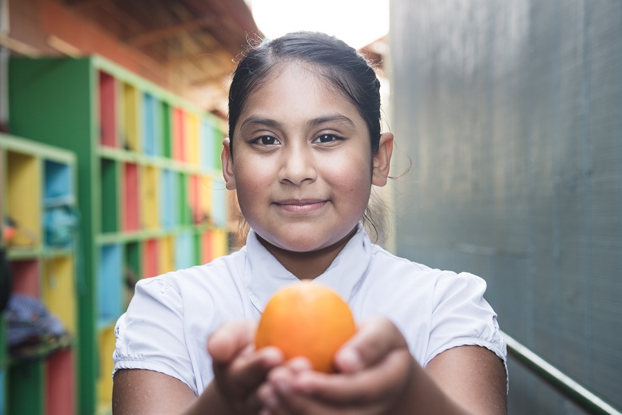 A little girl holds out an orange