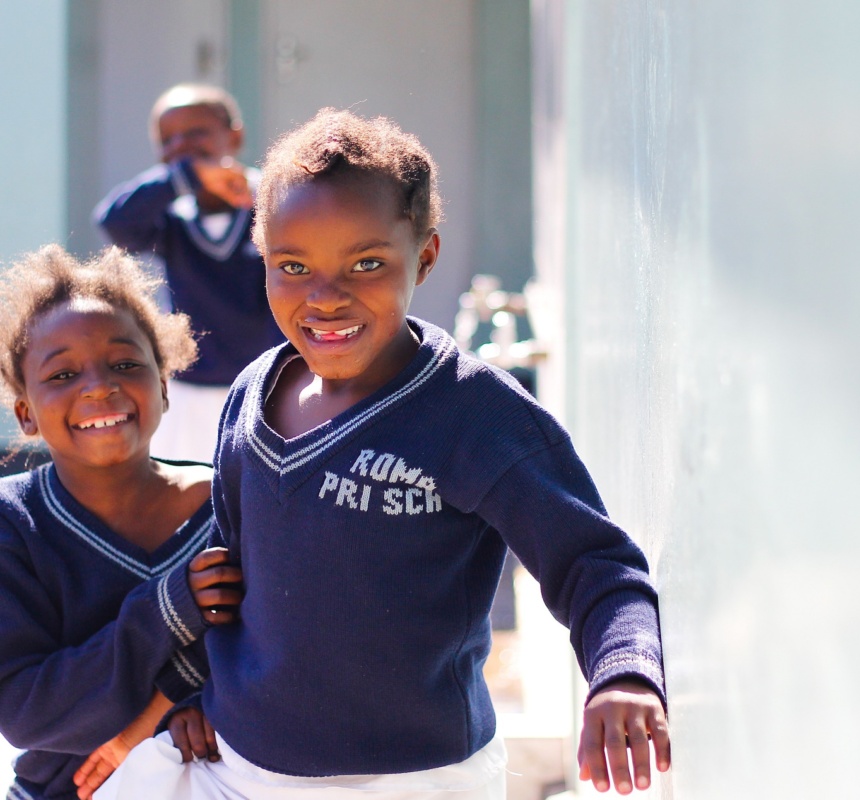 Three African children smile in the outdoor hallway of their school