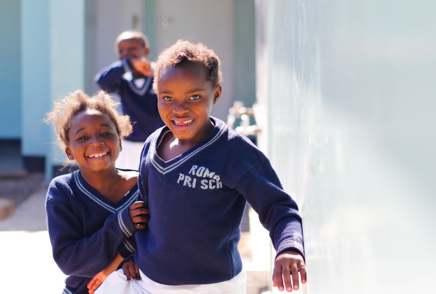 Three African children smile in the outdoor hallway of their school