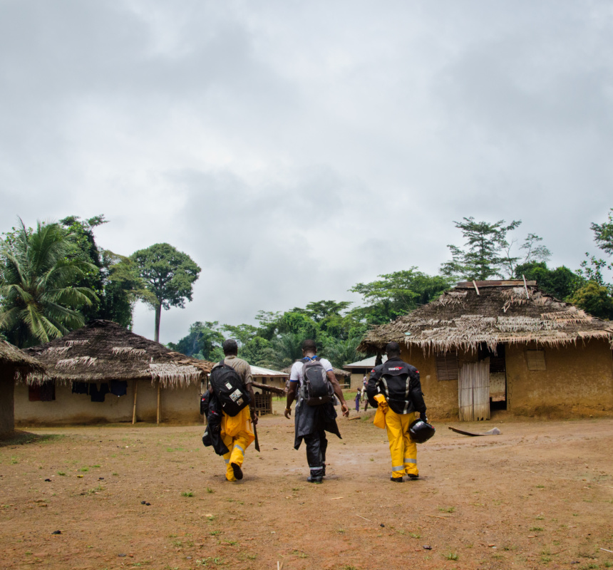 Three health workers walk along a dirt road