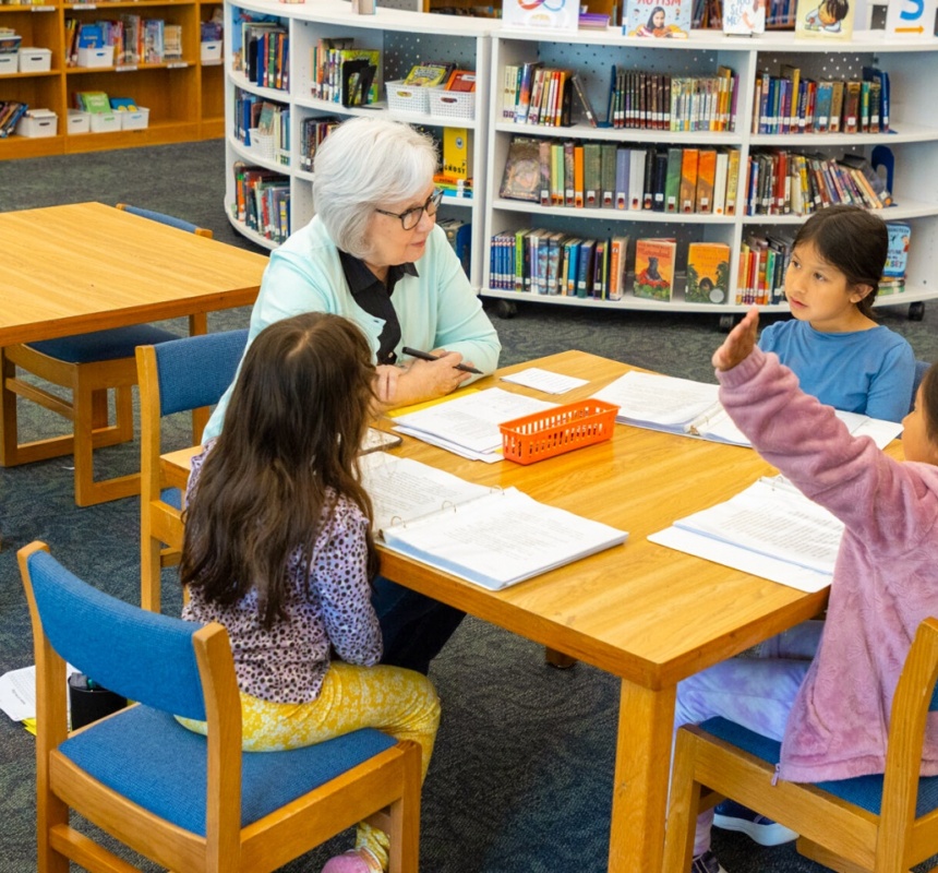 Three children sit in a library and work with a tutor