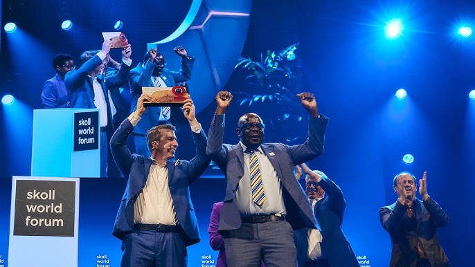 Lonnie Hackett and Ignicious Bulongo stand on stage at Skoll World Forum with their award raised in the air