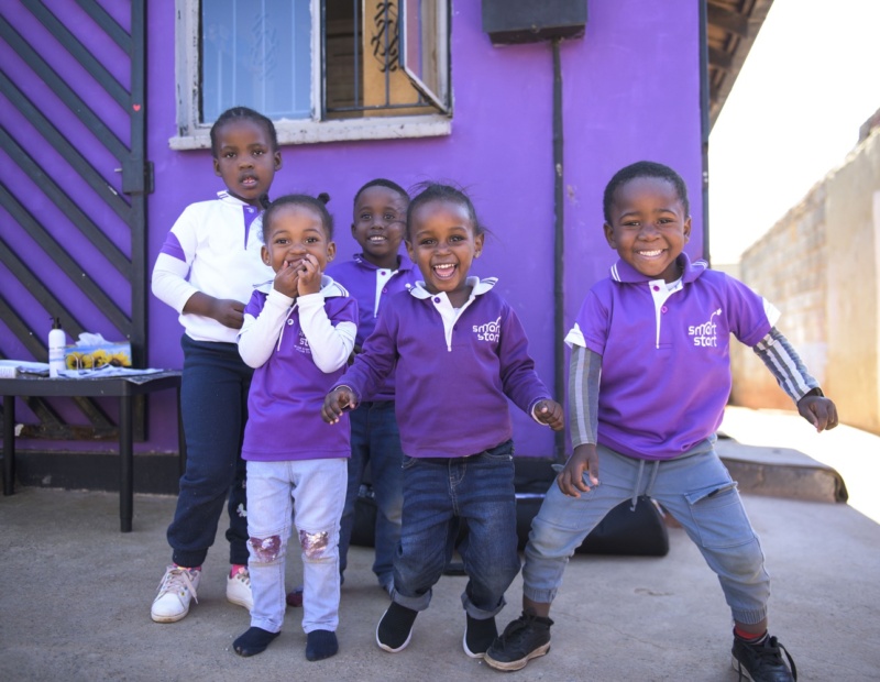 Five smiling African children dressed in purple reading SmartStart.
