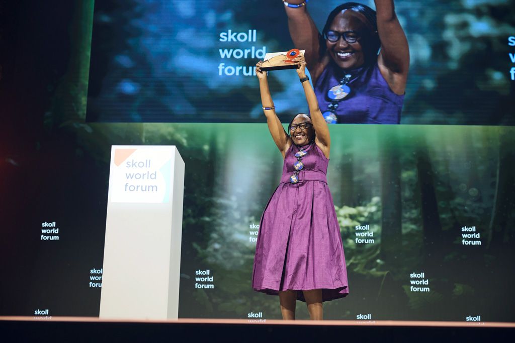 Grace Matlhape stands on the stage at the Skoll World Forum with her award raised above her head