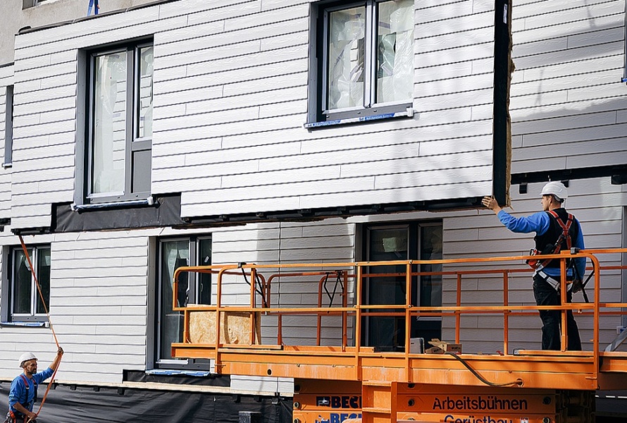 Two workers bring in specialized retrofitting equipment to the outside of a building