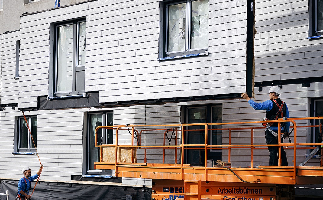 Two workers bring in specialized retrofitting equipment to the outside of a building